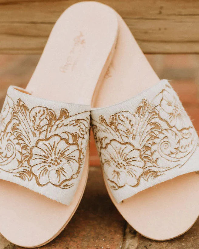 Pair of beige sandals with floral patterns on a stone surface